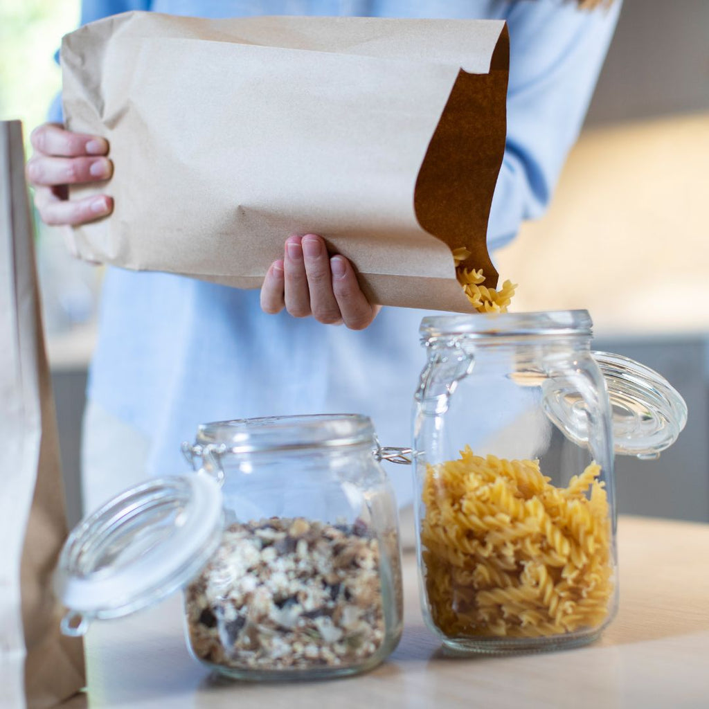 Refiling pasta from a paper bag into a glass jar
